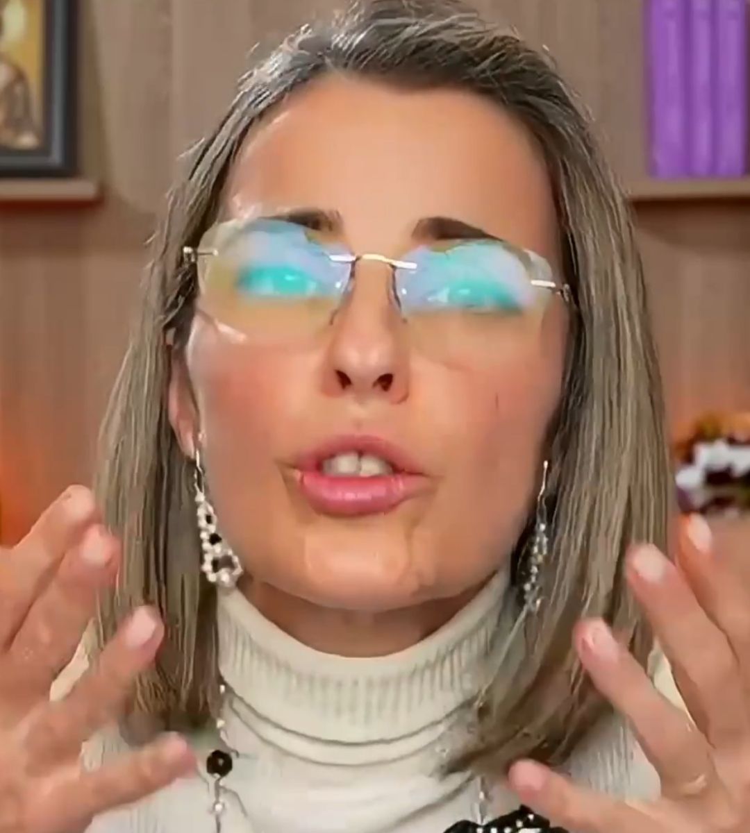Cristela Georgescu vorbește în timpul unui interviu online, purtând ochelari și un pulover alb, cu mâinile ridicate în fața camerei.
