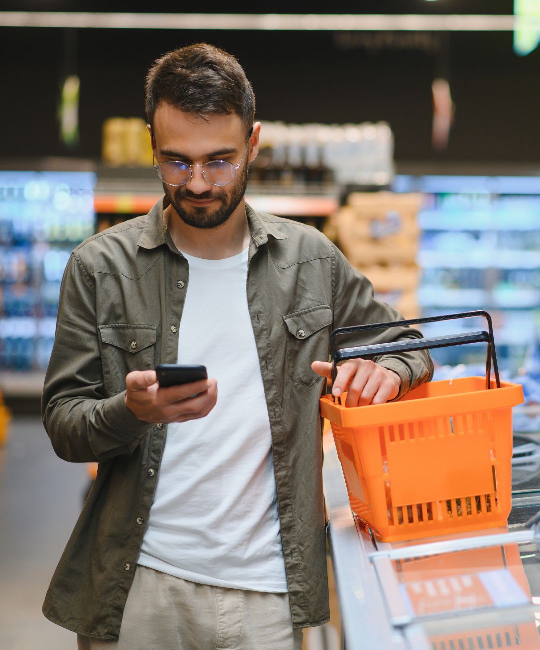 Cumpărător cu un coș portocaliu, verificând telefonul mobil într-un supermarket