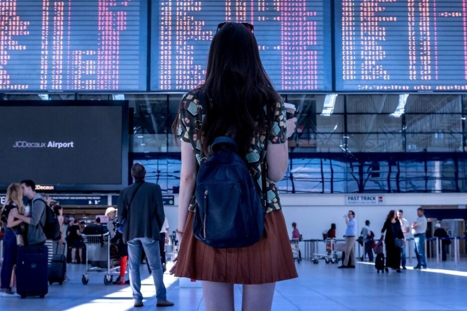 Femeie cu rucsac în fața panoului de zboruri dintr-un aeroport, fotografie ilustrativă
