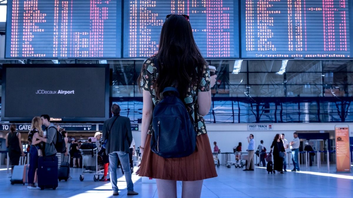 Femeie cu rucsac în fața panoului de zboruri dintr-un aeroport, fotografie ilustrativă